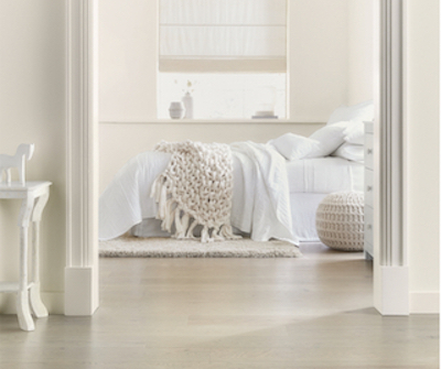 Entryway view into monochromatic neutral bedroom with crocheted throw and round pouf.