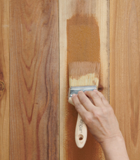 Mano con brocha que aplica tinte a un panel de madera.