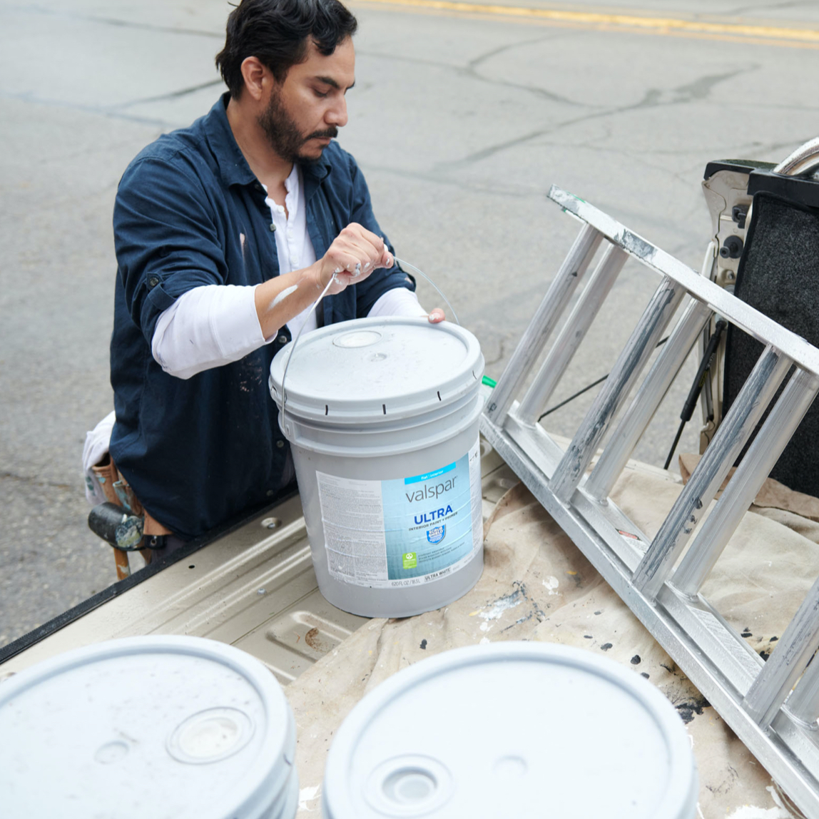 Pintor profesional carga 5 galones de Valspar® Ultra® en un paño en la plataforma del camión junto a una escalera.