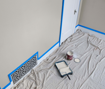 Paño junto a pared enmascarada. Pintura desteñida blanca y rodillo en bandeja. Lata abierta de pintura sin tapadera. 