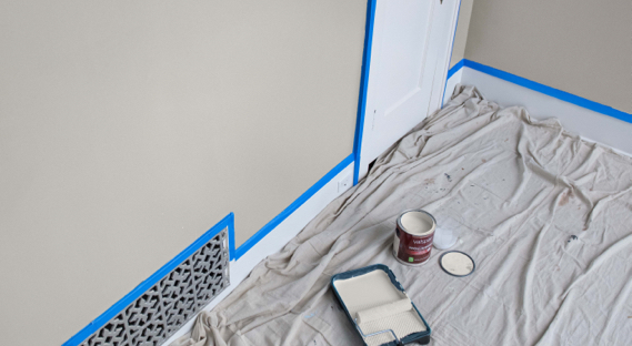 Paño junto a pared enmascarada. Pintura desteñida blanca y rodillo en bandeja. Lata abierta de pintura sin tapadera. 