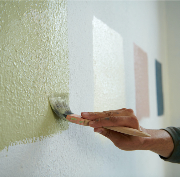 Mano que pinta un cuadrado de color en una pared con tres cuadrados de color en el fondo.