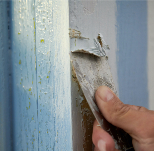 Acercamiento de mano usando un raspador para retirar pintura de una pared.