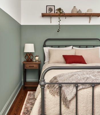 Recámara con mitad inferior de pared en Secret Moss y mitad superior en blanco neutral. Cama con postes de hierro con almohada rojo brillante.