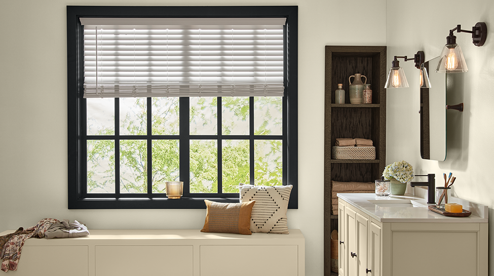 Baño con ventana, tocador, apliques de luz, cajón con almohadas en él, estante con toallas y vela sobre alféizar de ventana. 