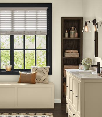 Baño con ventana, tocador, apliques de luz, cajón con almohadas en él, estante con toallas y vela sobre alféizar de ventana. 
