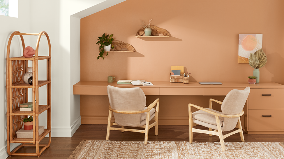 Habitación con un escritorio, dos sillas, plantas, obras de arte en un estante y un librero de tipo bambú.