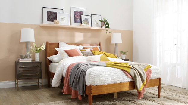 Cama cubierta con almohadas contra una media pared de color neutral arena con acento de color con estante que combina y lámparas modernas de mesa laterales.