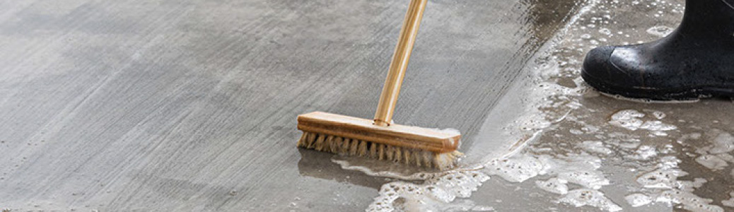 Escoba limpiando líquido del piso de concreto. Botas de goma en el fondo. 