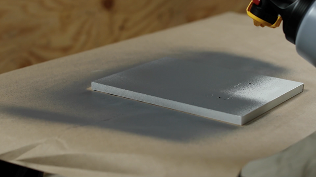 Rociador de pintura gris en tablero de madera blanco.
